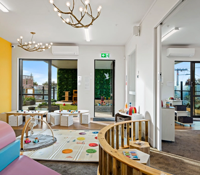 Light-filled activity space with child-height tables, open storage, and sliding glass opening to an outdoor deck