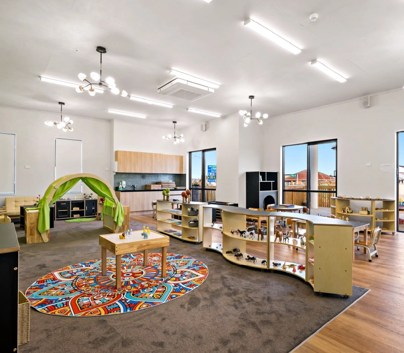 Play and learning zone with curved low shelving, fabric canopy nook, and timber kitchenette backdrop