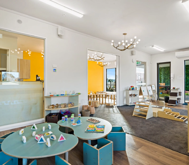 Large activity tables with cube seating, timber climbing frames, floor easels, and woven storage