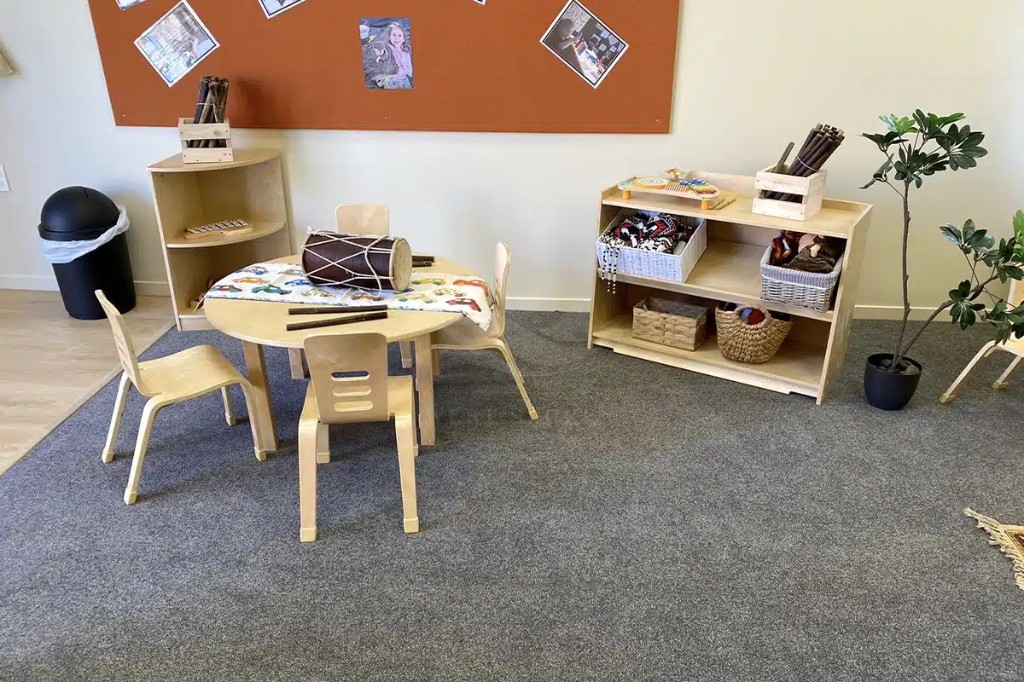 Music and circle-time zone with round child-height table, drum, and open shelving