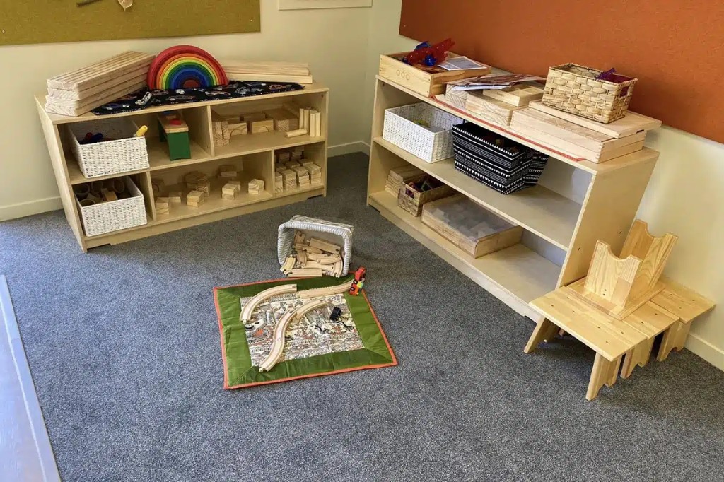 Block and small-world area with low cubby shelving and wooden train track on a play mat