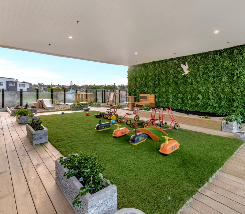 Covered rooftop deck with artificial turf, ride-on toys, small timber bridge, and living wall