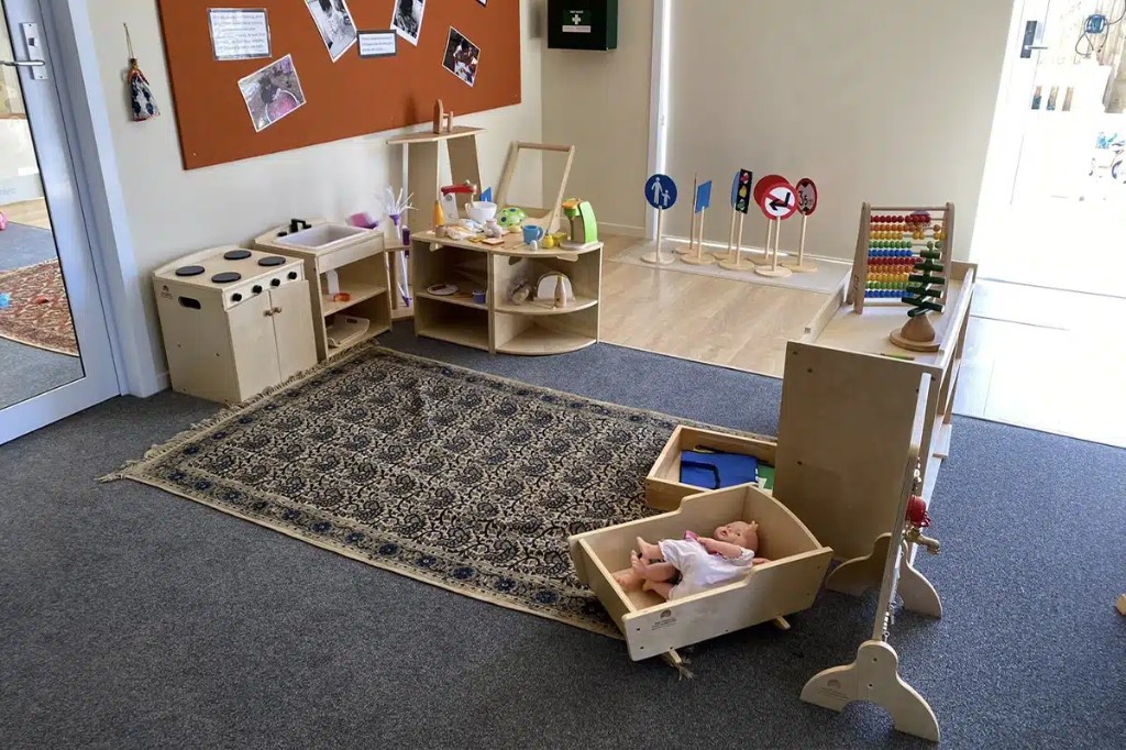 Dramatic play area with timber kitchen unit, shelving, and curated learning displays