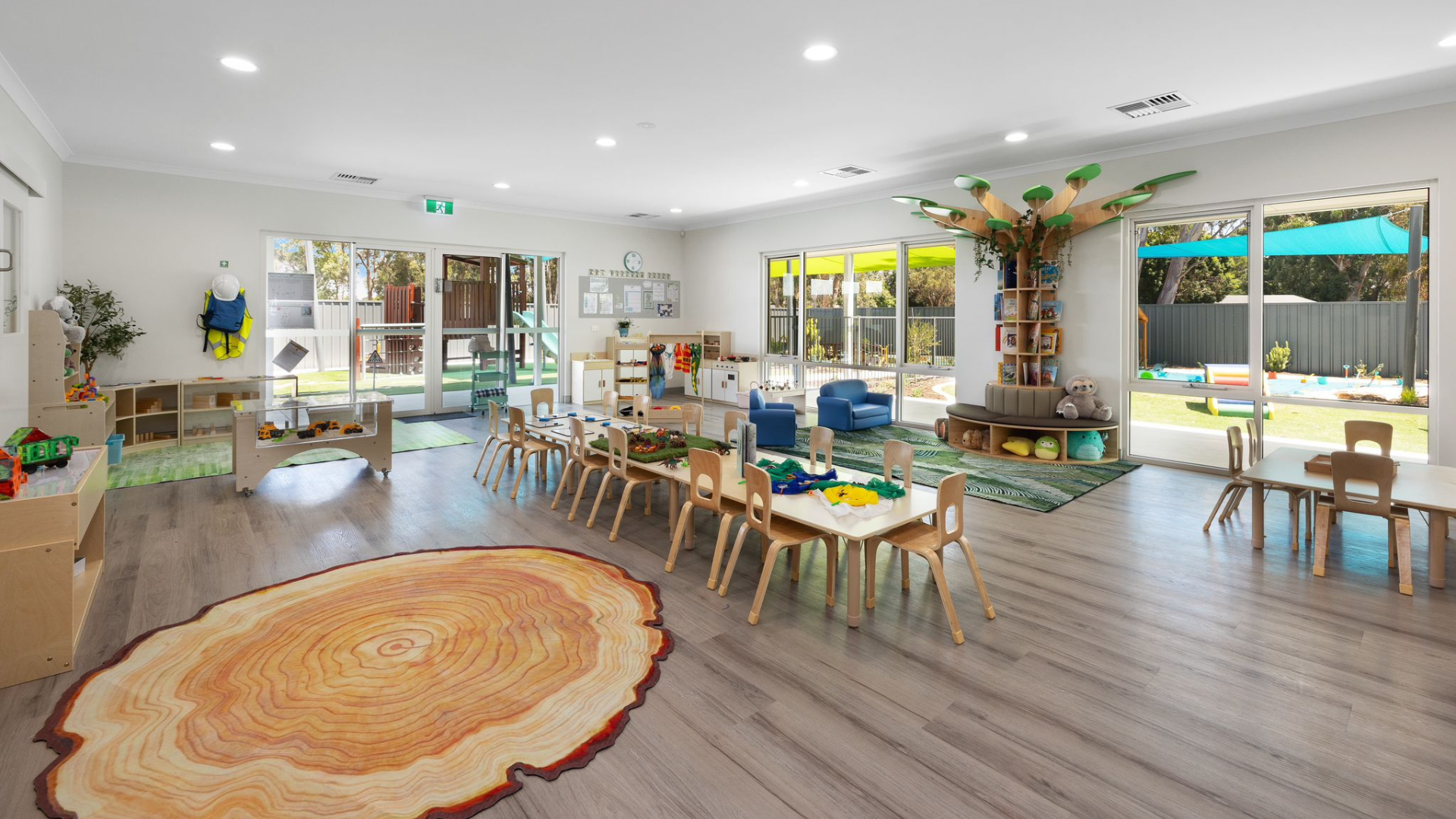 Bright early learning centre classroom with wooden tables, chairs, and shelving furniture
